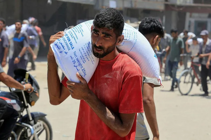 A Palestinian carries a sack of flour as people gather to receive aid supplies in Khan Younis, in the southern Gaza Strip, June 26, 2025. REUTERS/Hatem Khaled