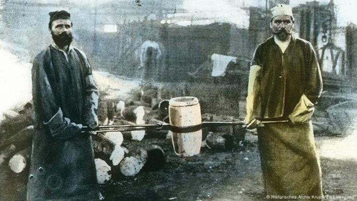 Foundrymen carry a melting pot with molten steel to the smelting furnace