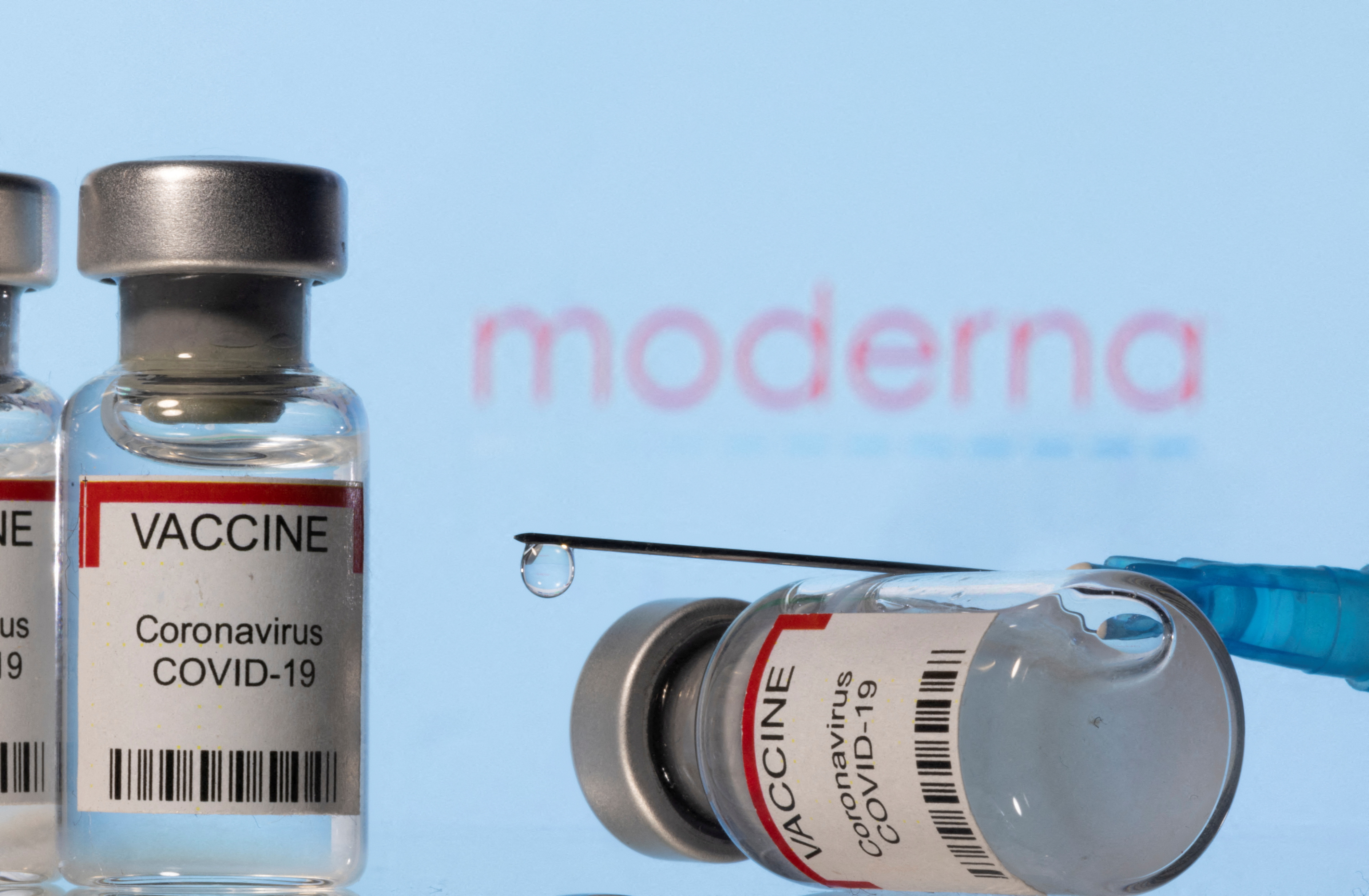 Illustration shows vials labelled VACCINE Coronavirus COVID-19 and a syringe in front of a displayed Moderna logo