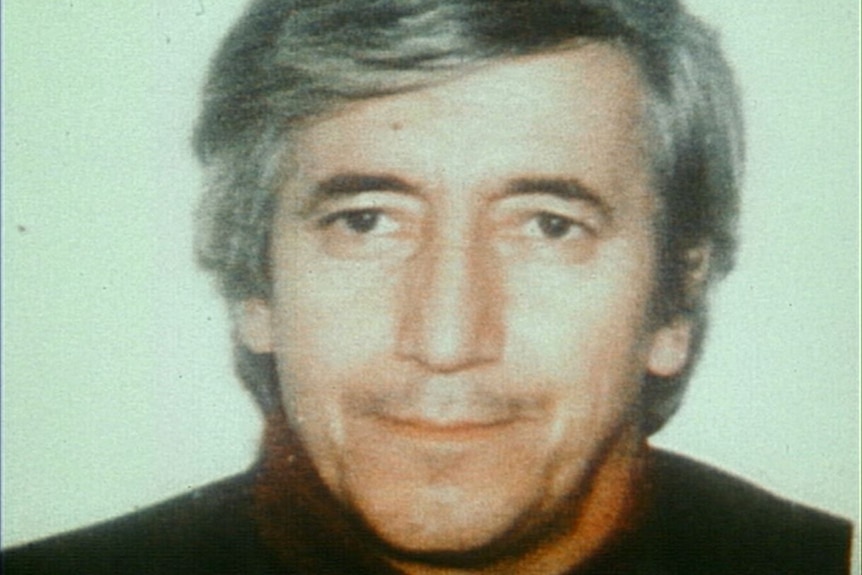 An archival photo of a man in his late forties with grey hair and a sweater on.