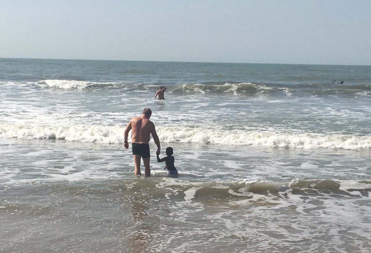  A tourist wades into the sea with a small African child in The Gambia - where child sex abuse is rife
